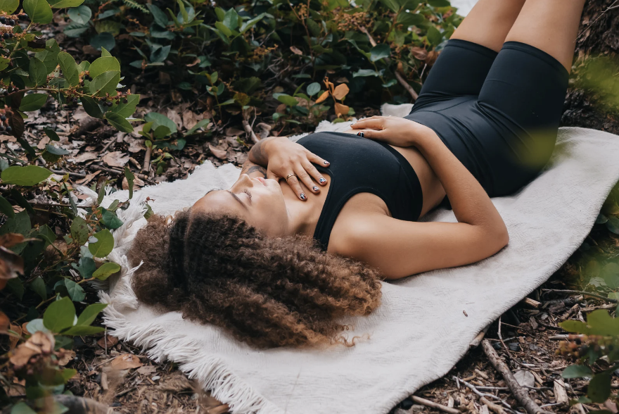 Woman practicing grounding techniques by lying on a blanket in nature, showcasing the mental health benefits explored through neuroscience.